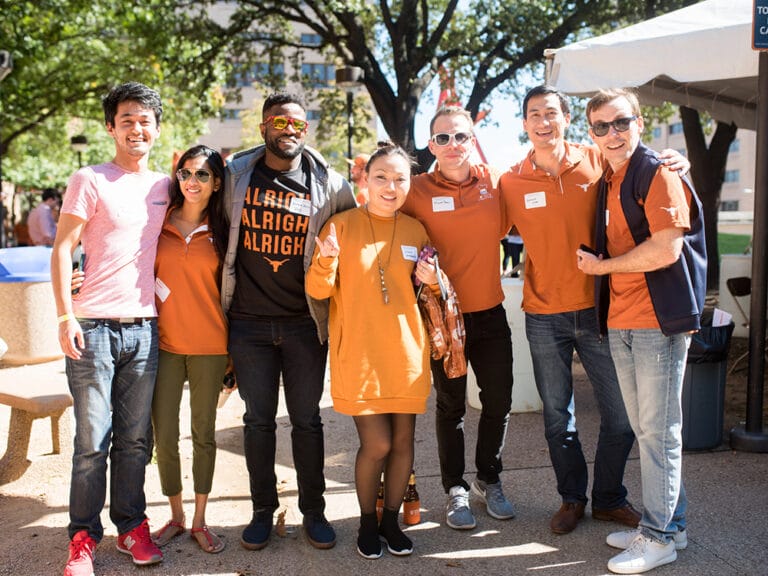 group of young alumni doing hook 'em horns hands