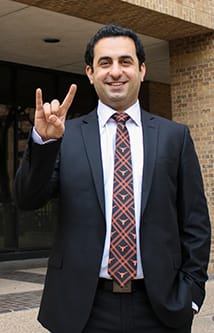 Eshkalak poses in a suit doing the hook 'em horns sign.